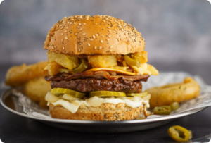 A mouthwatering hamburger featuring melted cheese, crunchy onion rings, and pickles, all nestled in a soft bun.