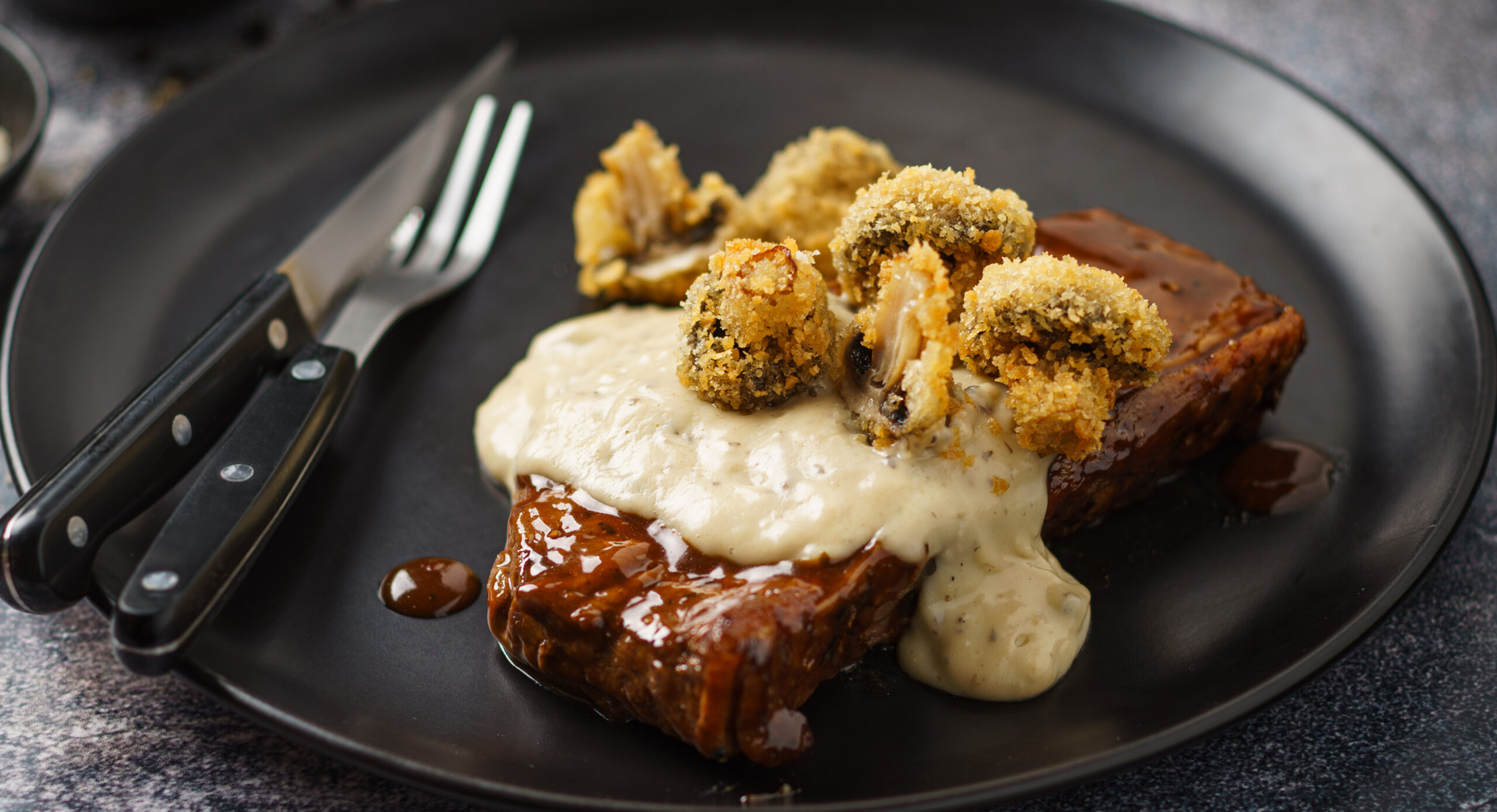 A succulent piece of meat topped with rich gravy and garnished with crispy fried mushrooms on a white plate.